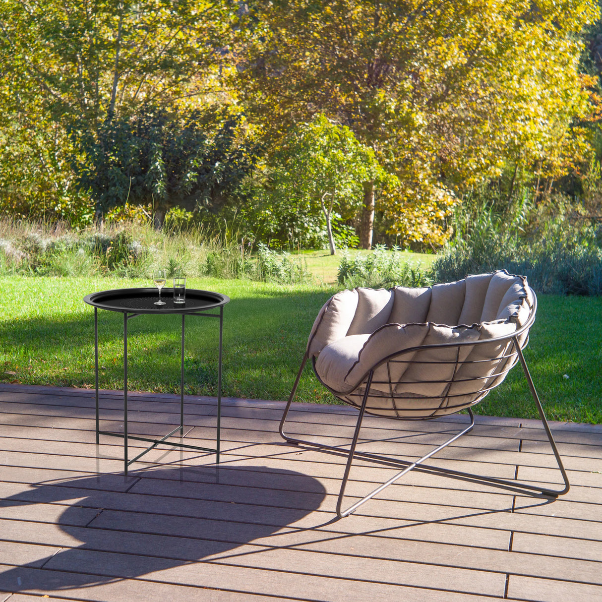 Schwarzer Beistelltisch ALLRUND aus Metall mit Lochmuster auf einer Terrasse neben einem Loungesessel von hjh LIVING