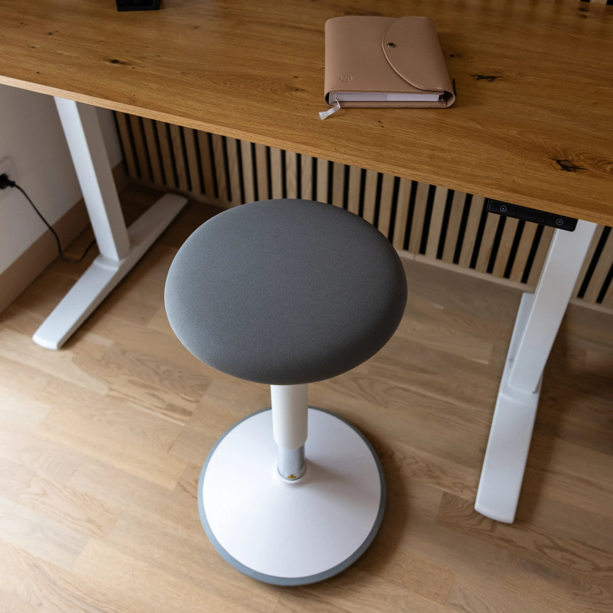 Grau gepolsterte Sitzfläche der Stehhilfe BALANCE SIT III W mit weißem Fußkreuz und zentraler Säule von hjh OFFICE