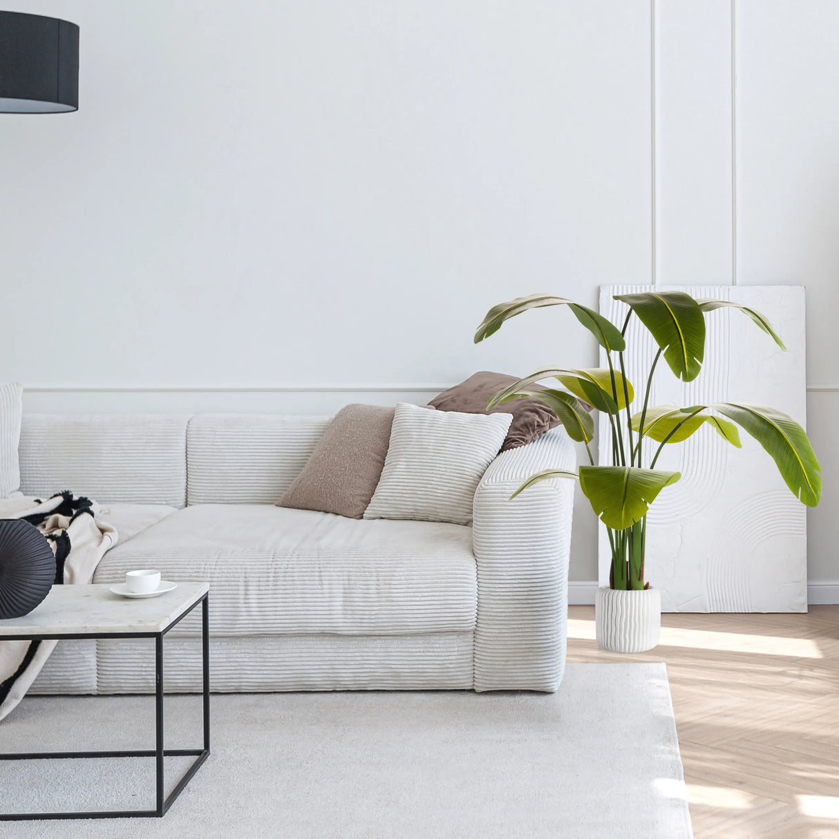 Grüne Kunstpflanze BANANE in einem weißen Übertopf neben einem Sofa von hjh OFFICE
