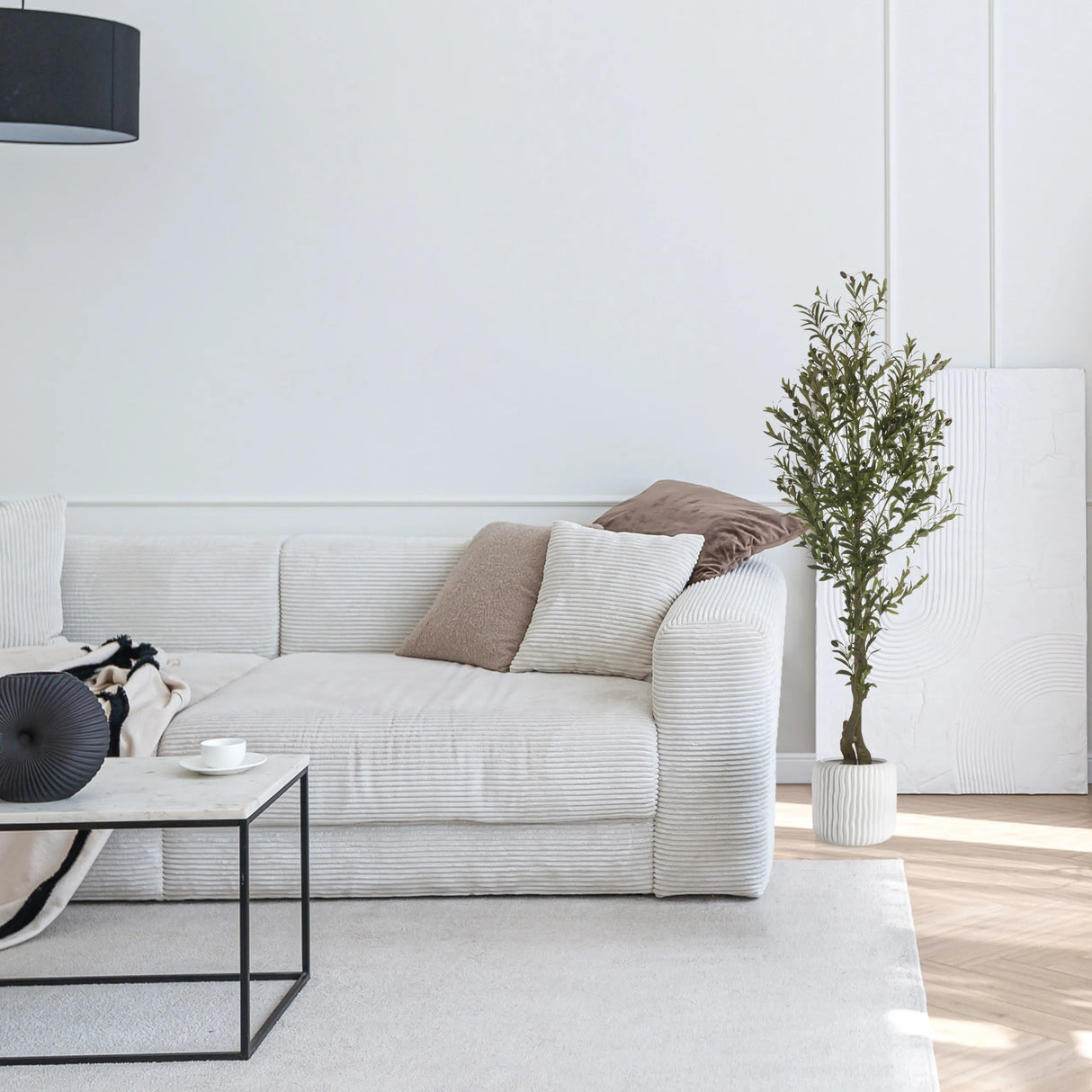 Grüne Kunstpflanze OLIVE I in einem weißen Topf neben einem hellen Sofa von hjh OFFICE