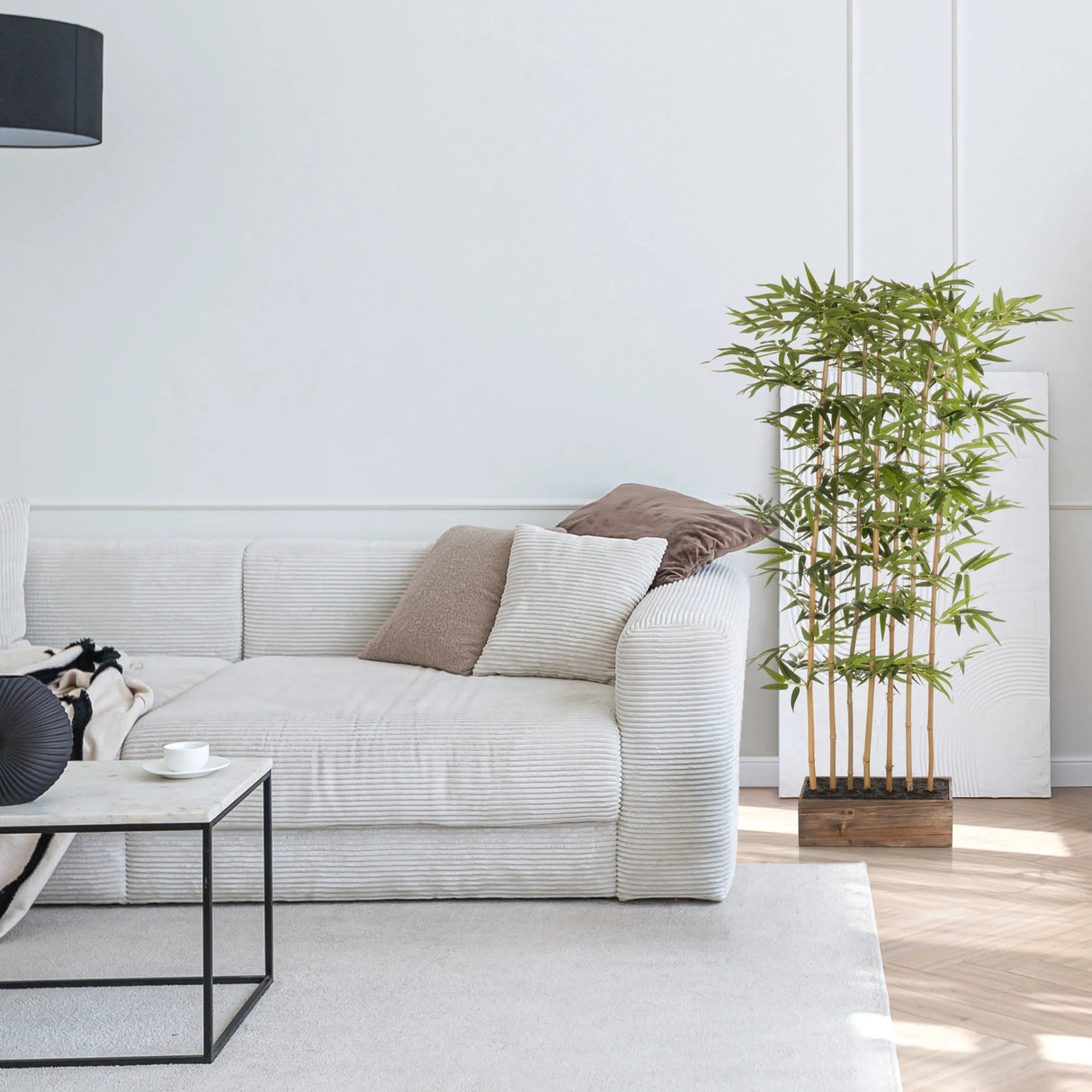 Grüne Kunstpflanze BAMBUS I in einem Holzgefäß neben einem weißen Sofa von hjh OFFICE