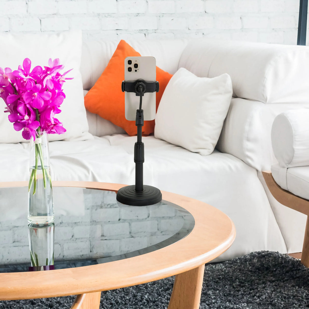 Schwarze Handy- und Tablet-Halterung FLEXMOBI II mit Smartphone auf einem Glastisch vor weißem Sofa von hjh OFFICE