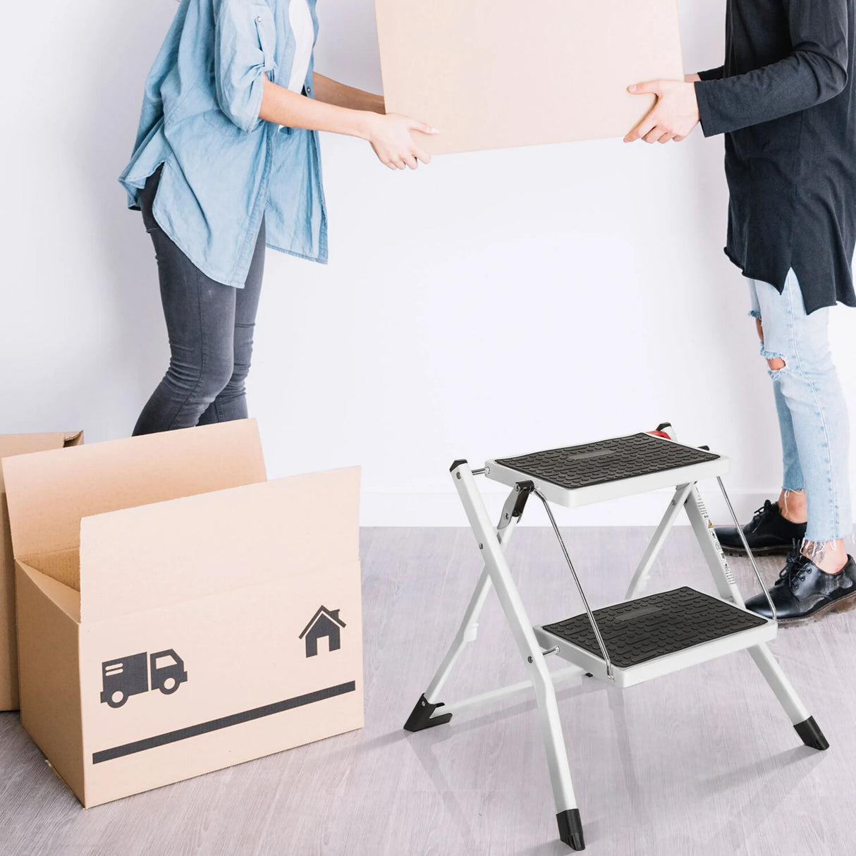 Weiße Klappleiter SOLID W1 mit zwei schwarzen Stufen neben einem Umzugskarton von hjh OFFICE