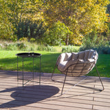 Schwarzer Beistelltisch ALLRUND aus Metall mit Lochmuster auf einer Terrasse neben einem Loungesessel von hjh LIVING