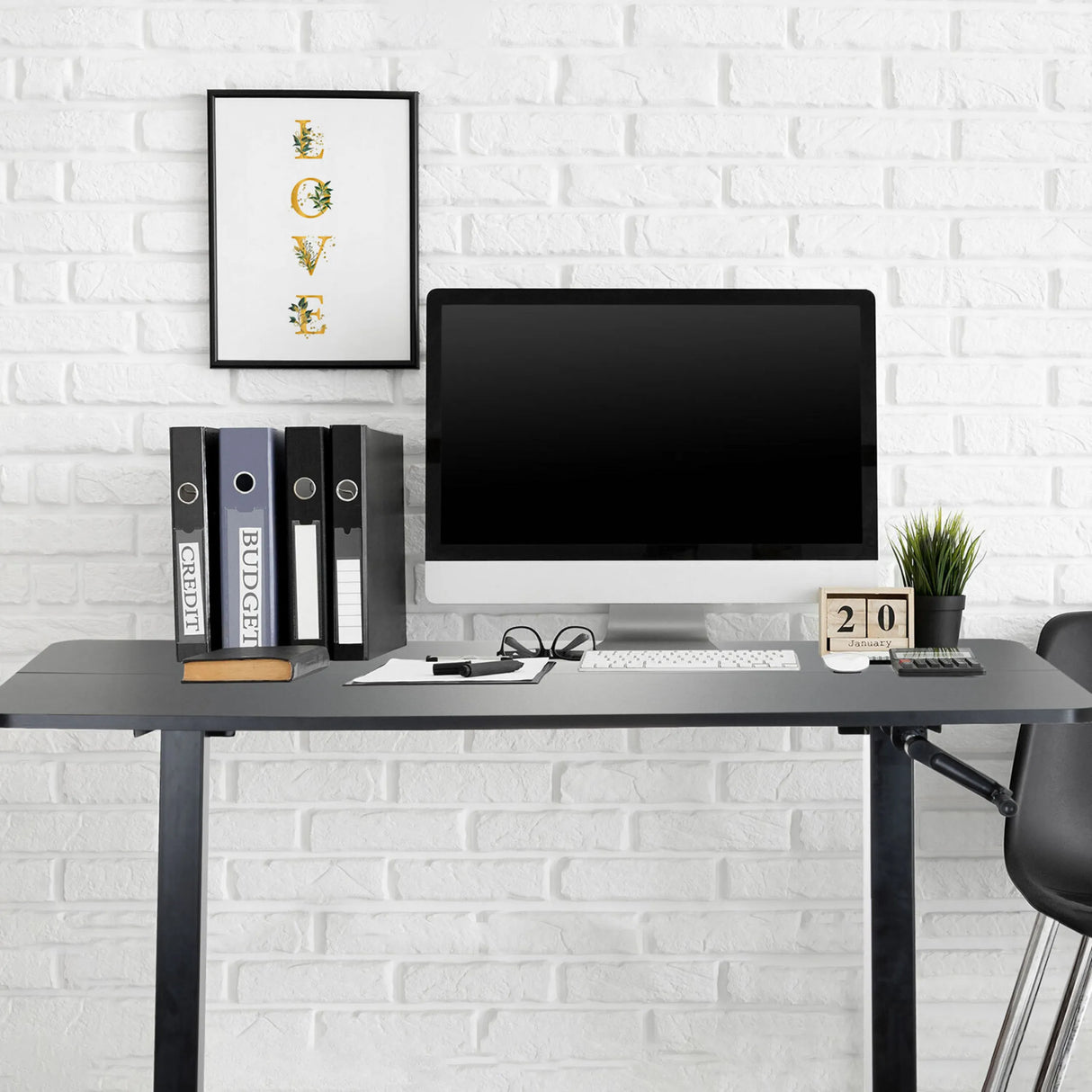 Schwarzer Stehschreibtisch STAND CR mit Monitor, Tastatur und Aktenordnern vor einer weißen Ziegelwand von hjh OFFICE