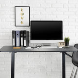 Schwarzer Stehschreibtisch STAND CR mit Monitor, Tastatur und Aktenordnern vor einer weißen Ziegelwand von hjh OFFICE