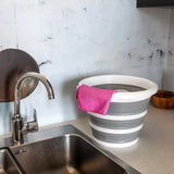Grau-weißer Faltbehälter CLEAN SILR mit einem rosa Tuch auf einer Arbeitsfläche neben einem Waschbecken von hjh OFFICE