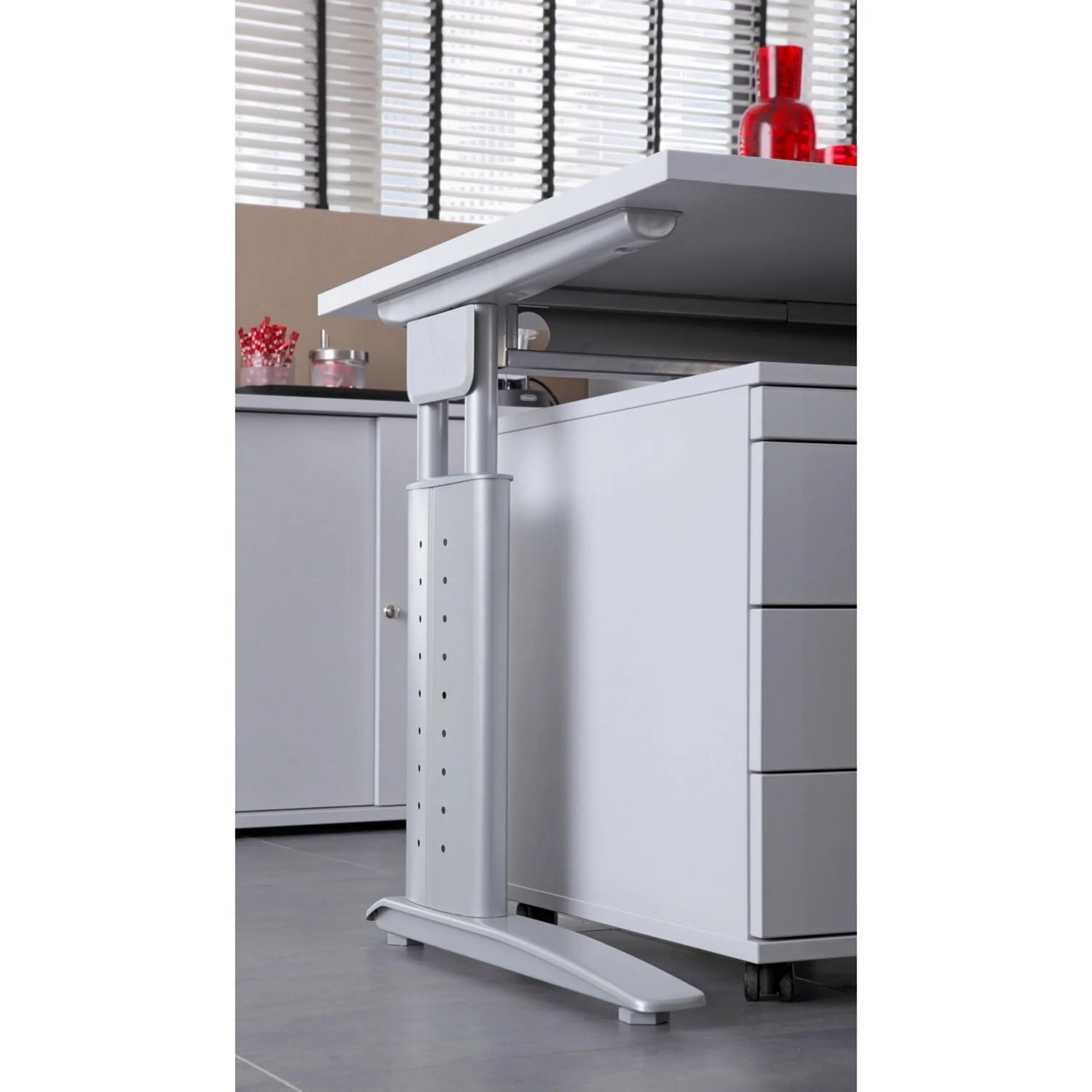 Höhenverstellbares Gestell in Silber des Schreibtischs UNDA 18 S neben einem grauen Rollcontainer von hjh OFFICE PRO