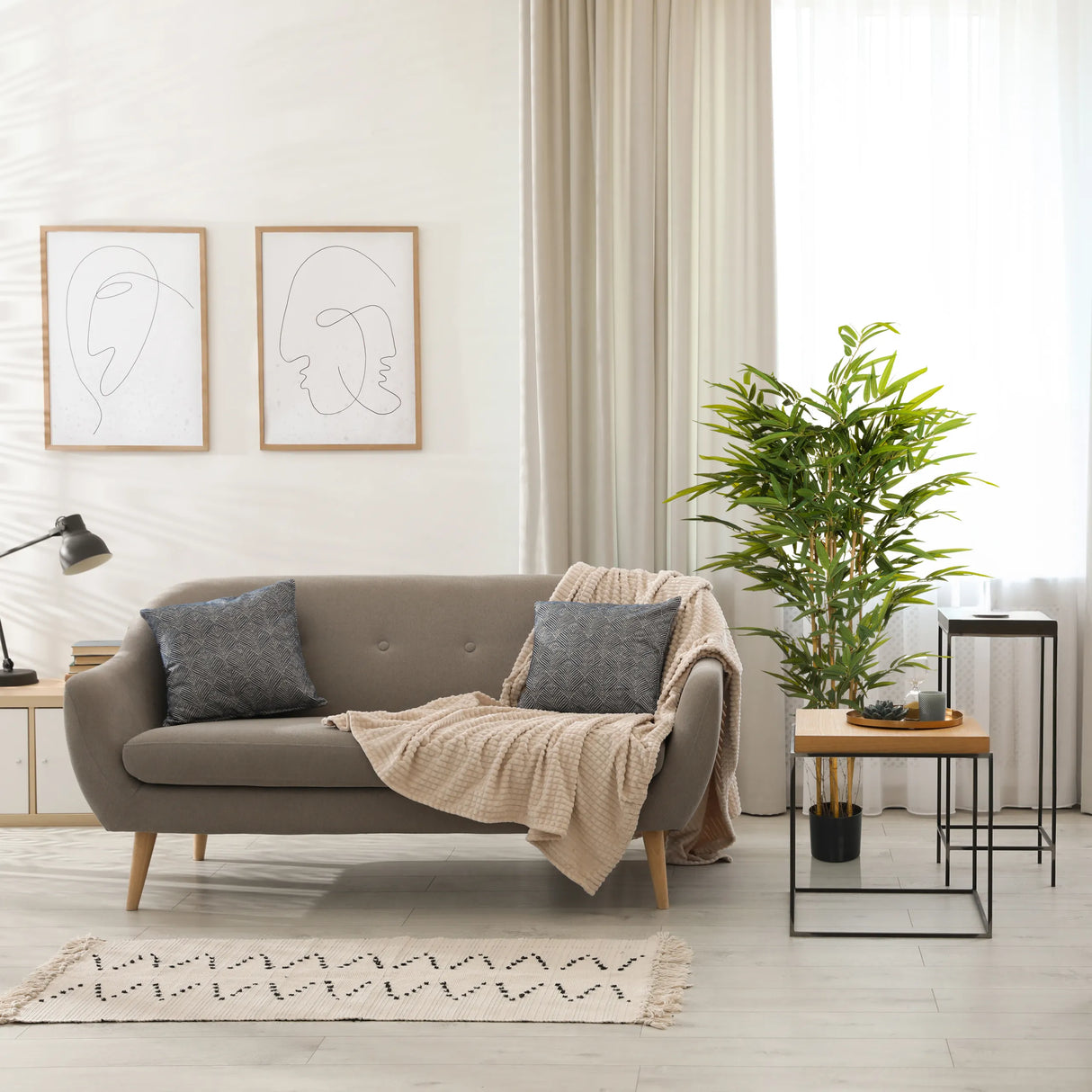 Grüne Kunstpflanze BAMBUS II in einem schwarzen Topf neben einem Sofa von hjh OFFICE